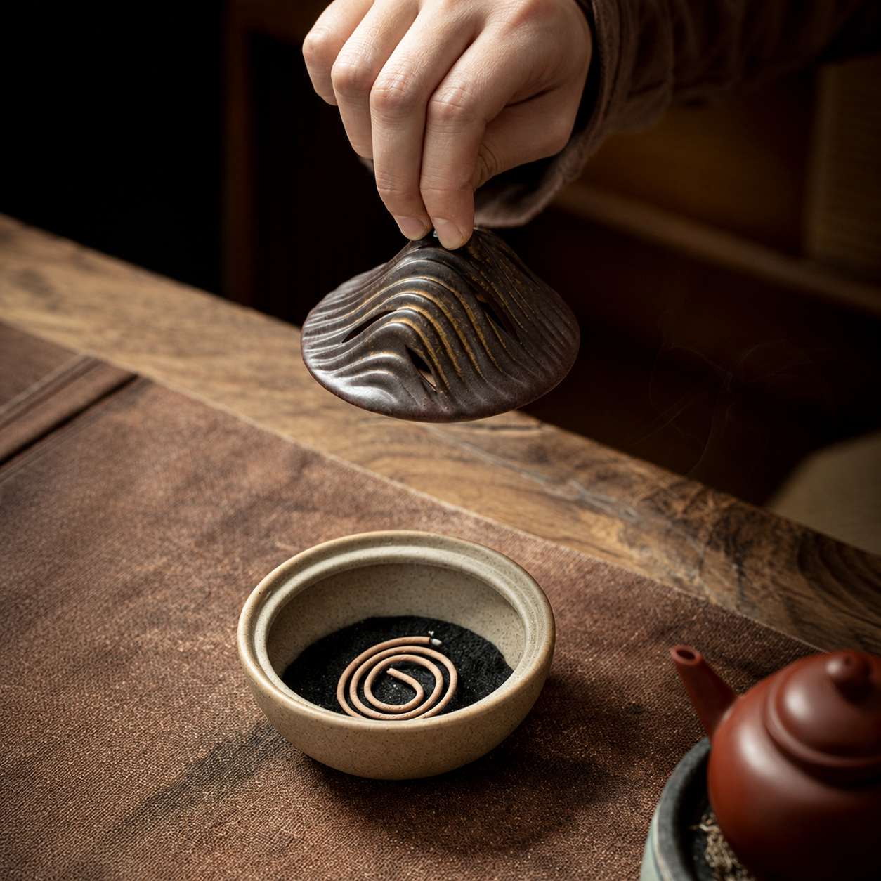 Hand lifting mountain lid from ceramic incense burner with coil incense inside