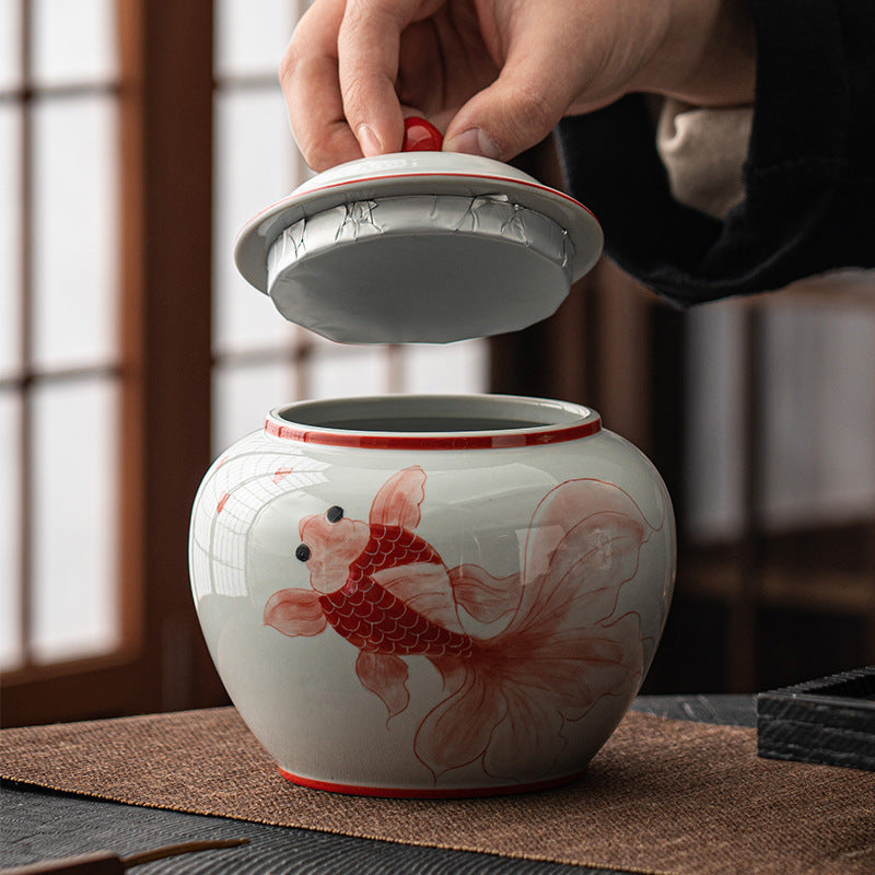 Red goldfish ceramic tea caddy jar with removable lid lifted by hand