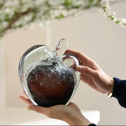 Side profile of amber and clear glass apple held in hands