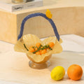 Amber art glass basket with blue handle filled with fruit