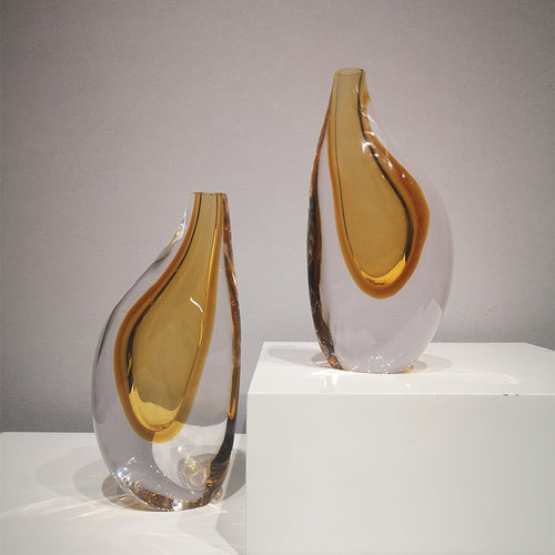 Two asymmetric amber glass vases on a white pedestal