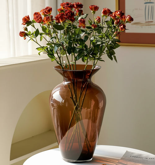 Amber glass flared vase holding a bouquet of red and orange roses