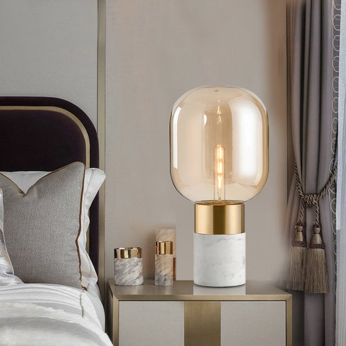 Amber glass table lamp with white marble base styled on a modern bedside table with soft lighting