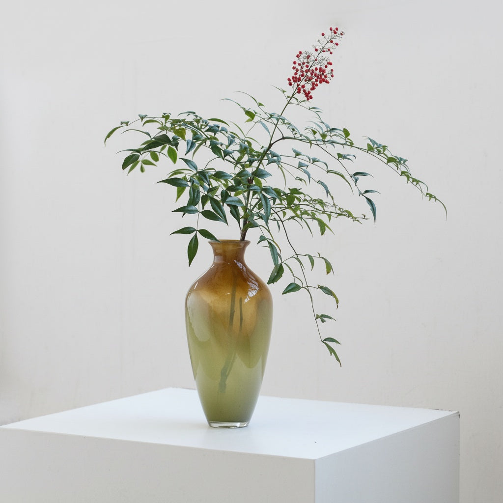 Gradient glass vase styled with a leafy red berry branch on a white plinth