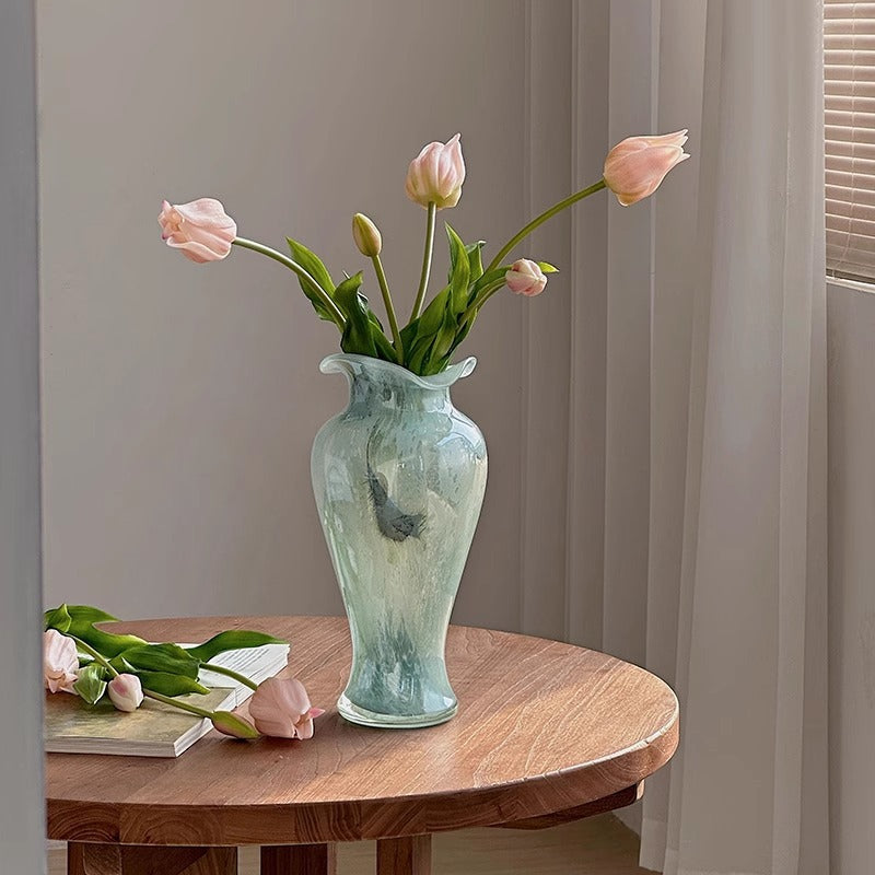 Aqua art glass vase holding pink tulips on wooden table