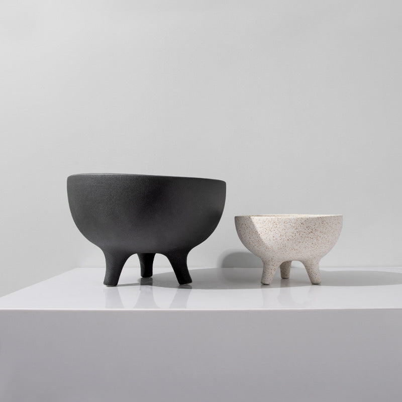 Artisan ceramic tripod vessels in charcoal matte and speckled mineral tones displayed on a white minimalist surface