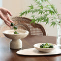 Beige marble bowl and oval tray set on wooden table with greenery