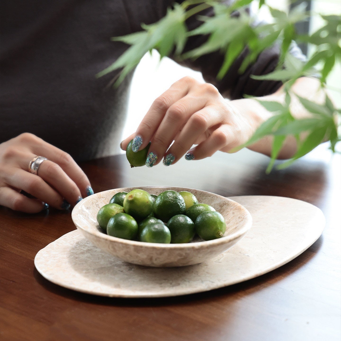 Hand reaching for lime in beige marble bowl on oval tray