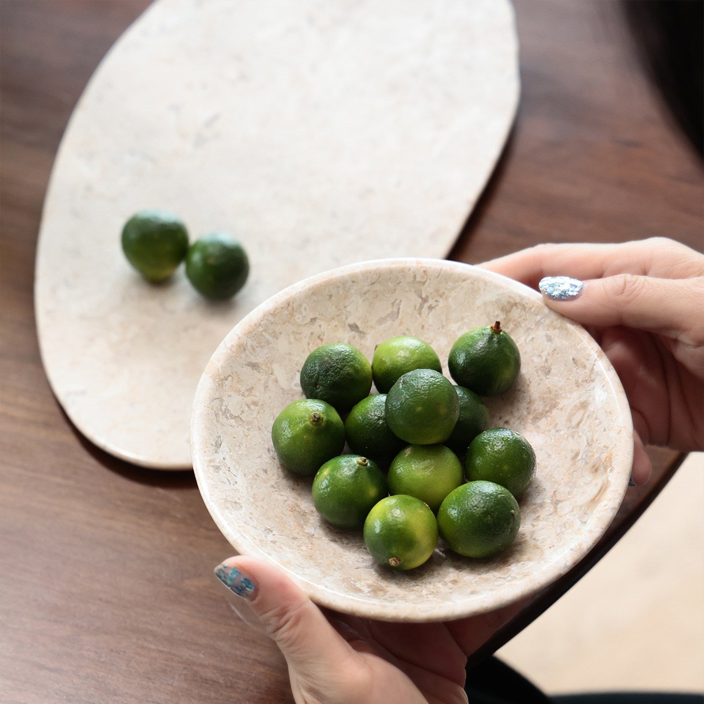 Hands holding beige marble bowl with oval tray in background