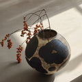 Textured ceramic round vase with abstract black spots holding dried branches