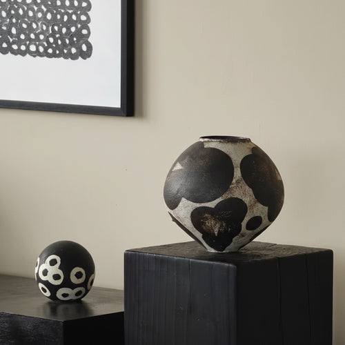 Black and beige spotted ceramic vase displayed on a black pedestal