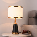 Front view of lit black and brass table lamp on marble table