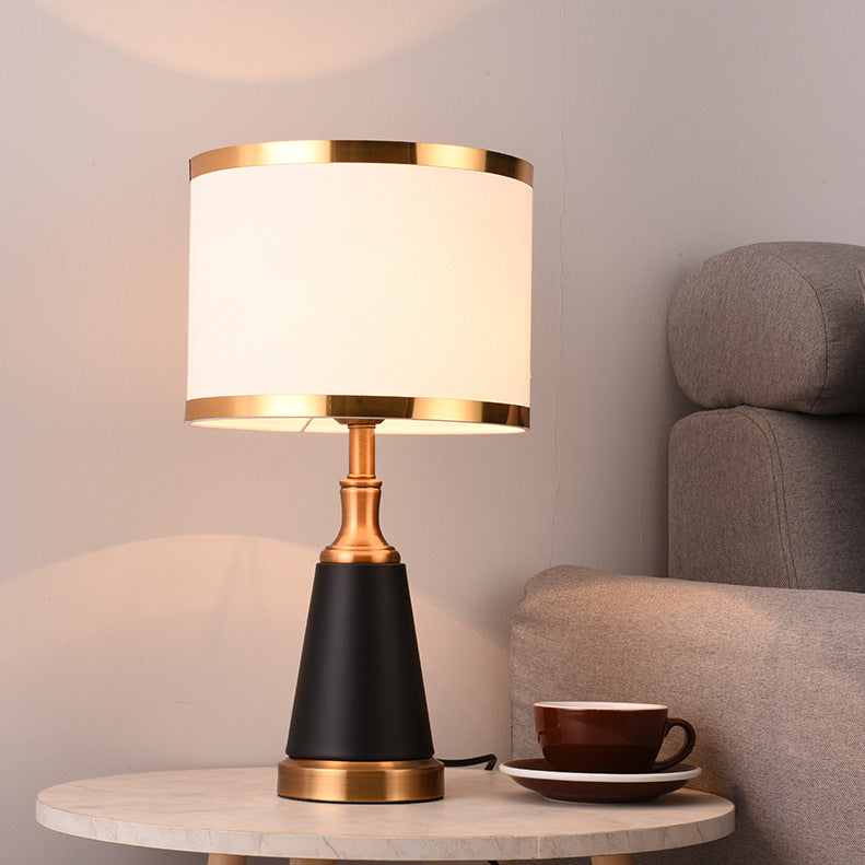 Front view of lit black and brass table lamp on marble table