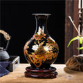 Front view of black ceramic vase with gold floral details on wooden stand