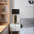 Black ceramic cylinder lamp with gold trellis overlay on bedside table