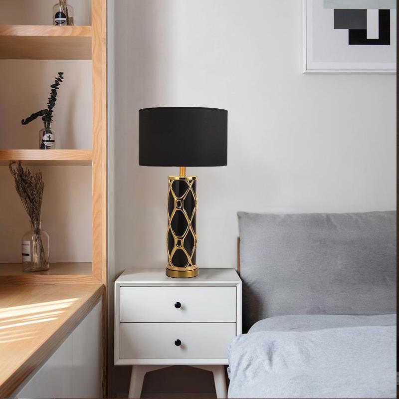 Black ceramic cylinder lamp with gold trellis overlay on bedside table