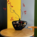 Illustrated black ceramic vase with red berry branches on table