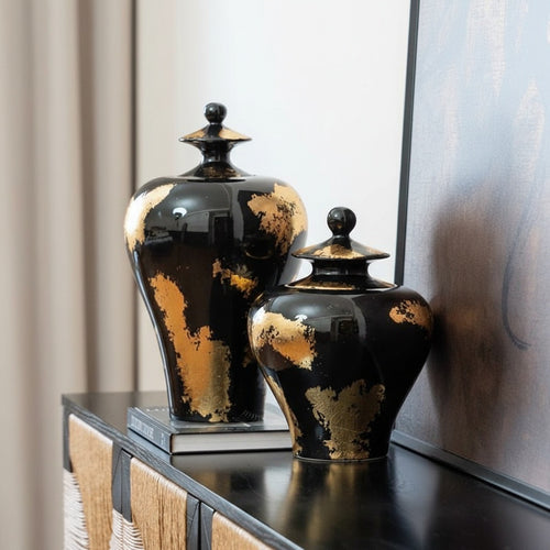 Two black and gold ceramic jars styled on a console table