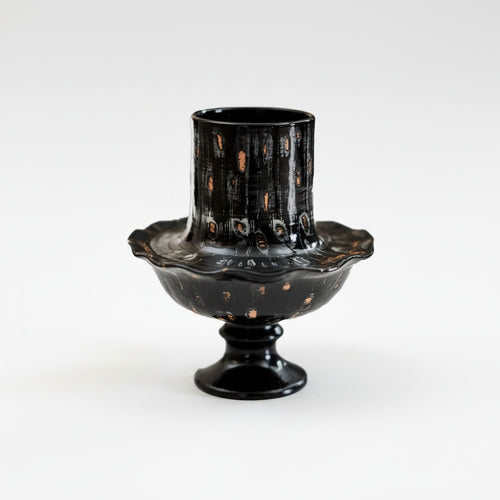 Front view of black and gold ceramic pedestal vase on white background