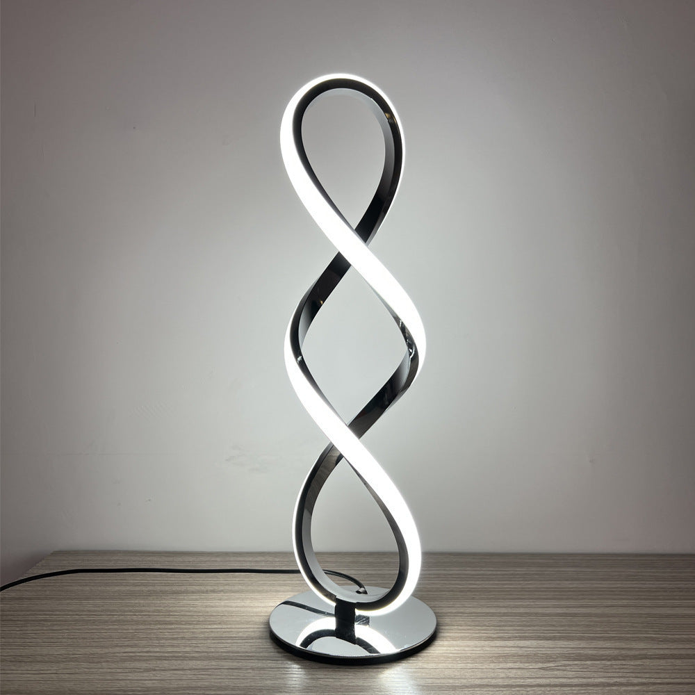 Illuminated black metal spiral LED table lamp on wooden surface