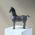 Side profile of black and white patterned horse sculpture on white pedestal