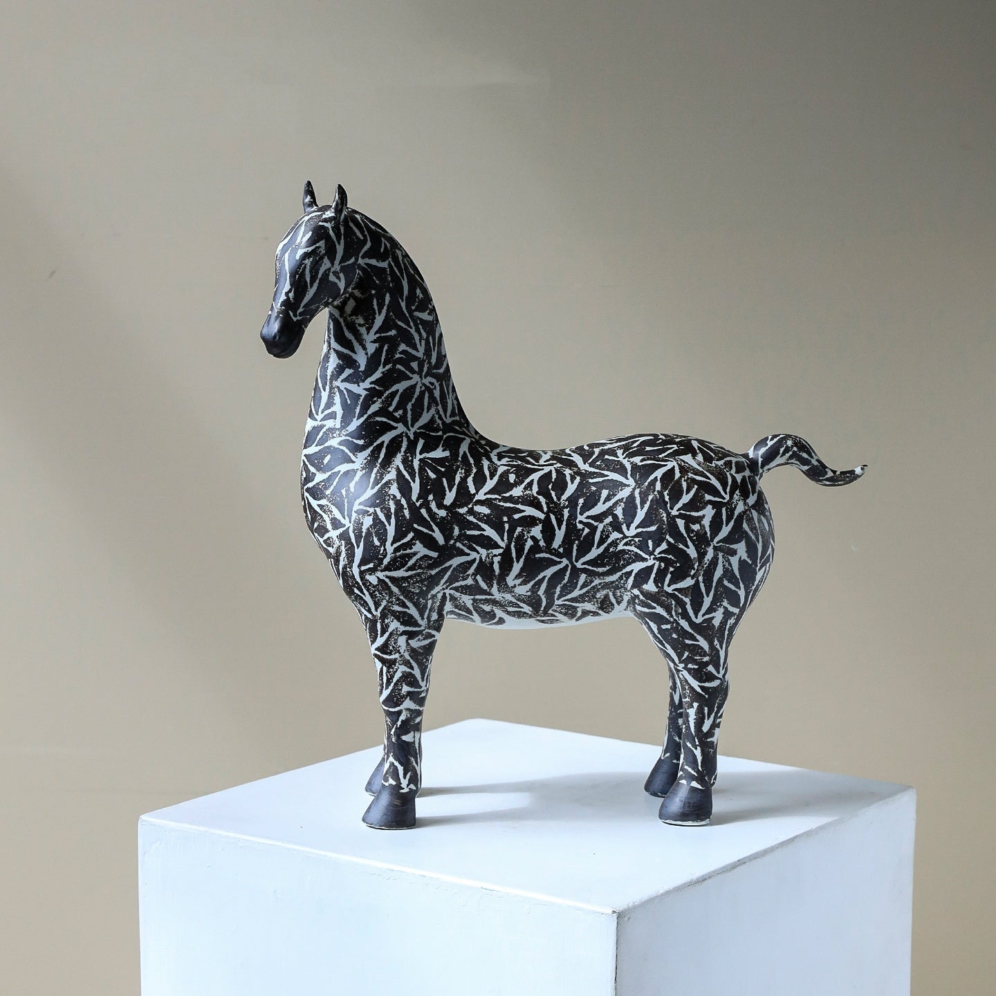 Side profile of black and white patterned horse sculpture on white pedestal