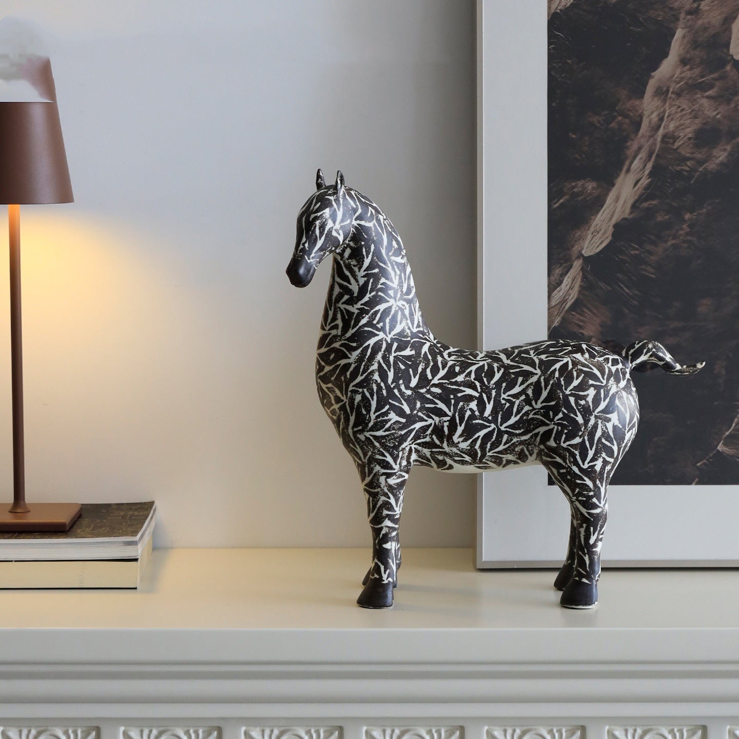 Patterned horse sculpture styled on shelf next to lamp and framed art