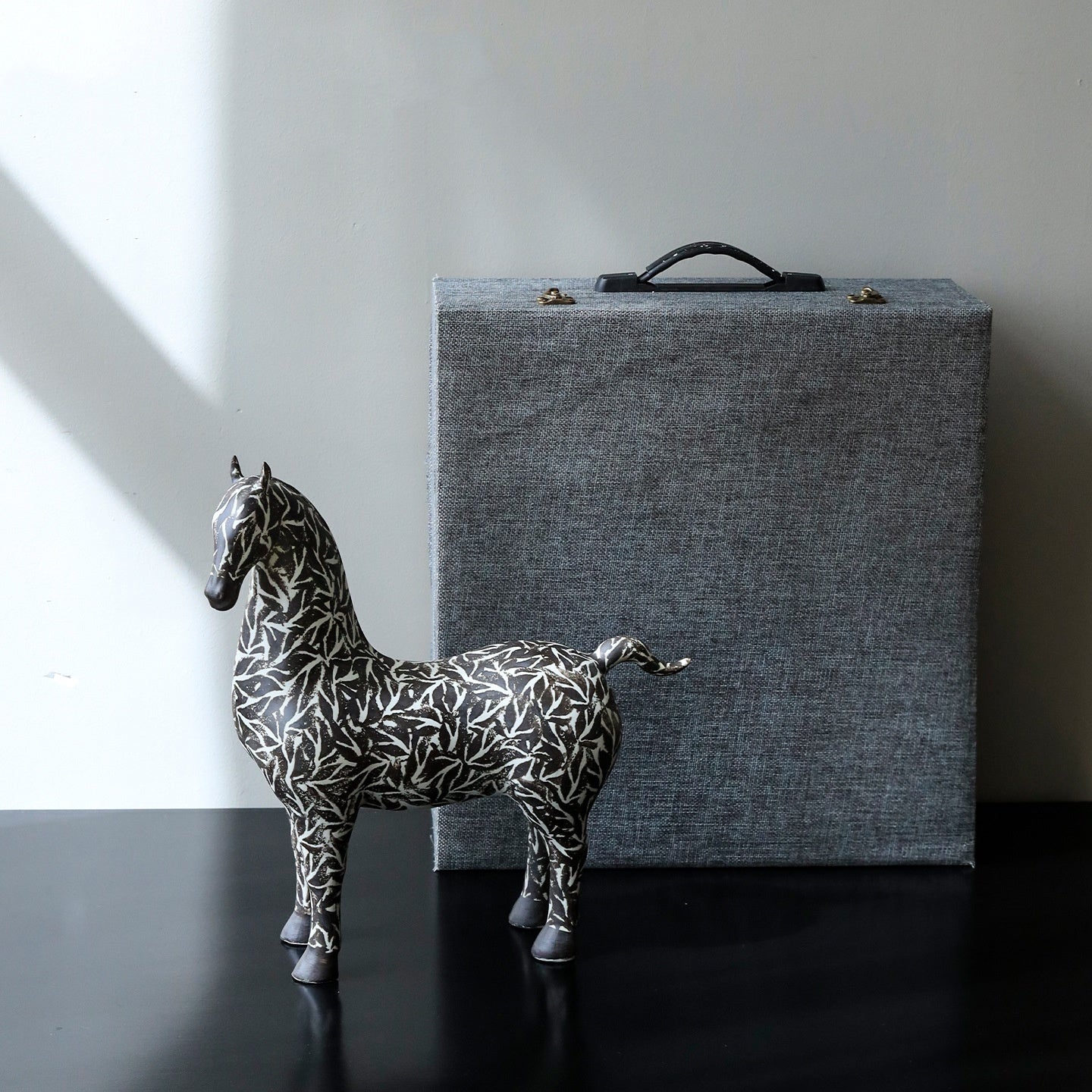Black and white horse statue on dark table next to grey storage box