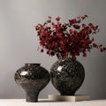Two black and white speckled ceramic vases with red flowers on a book