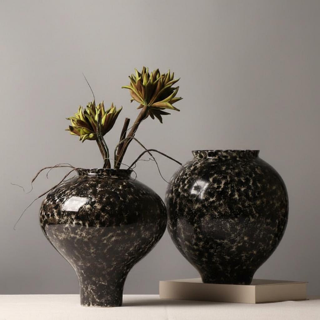 Pair of mottled black ceramic vases with dried green botanicals