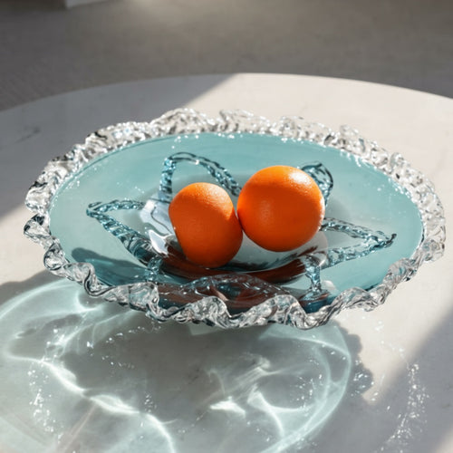 Translucent blue glass fruit bowl with oranges on marble table