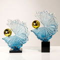 Front view of blue glass abstract wave sculpture with gold sphere on black base