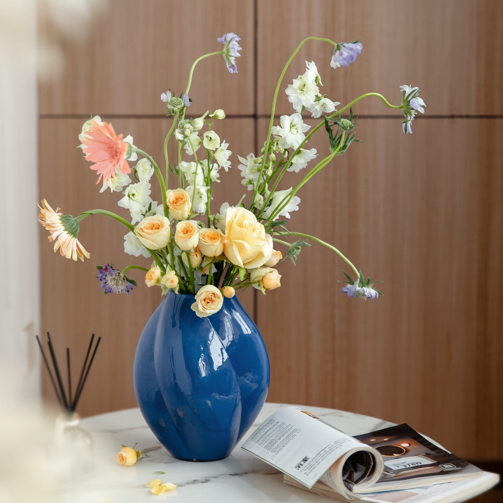 Glossy blue vase with mixed floral arrangement on coffee table