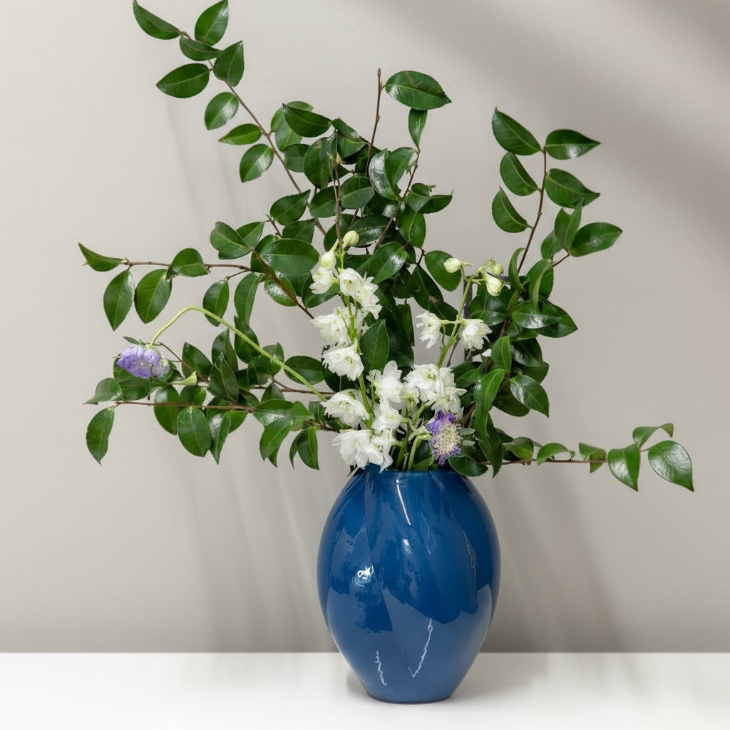 Blue glass vase with greenery and white flowers