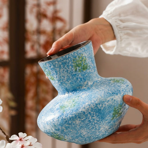 Hands holding blue and green speckled stoneware vase