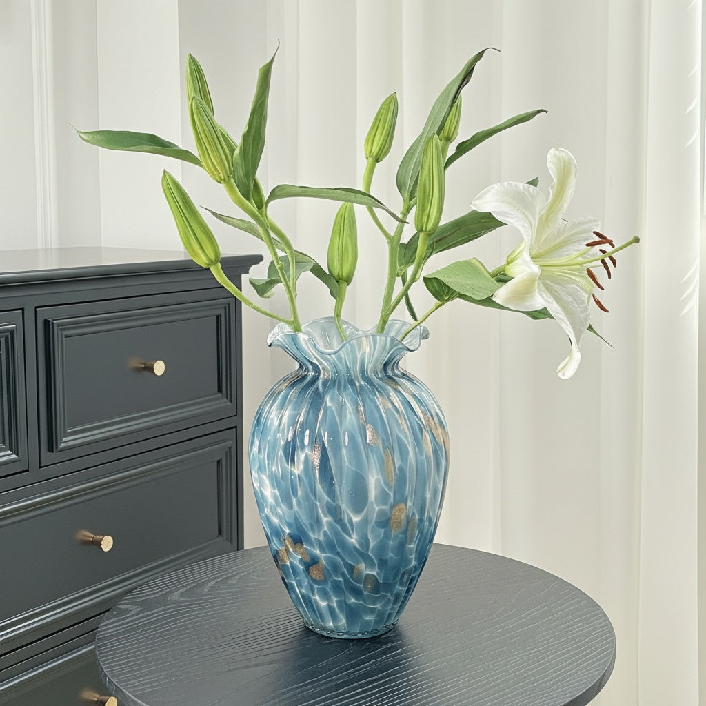 Blue art glass vase styled with green stems on modern black side table