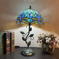 Illuminated blue stained glass dragonfly table lamp with bronze finish vine base on dark table