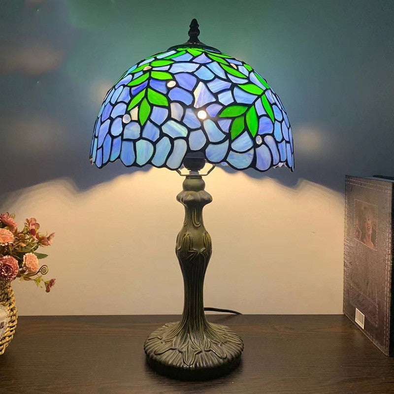 Lit blue stained glass table lamp with floral pattern and antique bronze base
