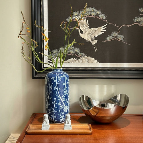 Cylindrical blue porcelain vase with white flowers and crane artwork background