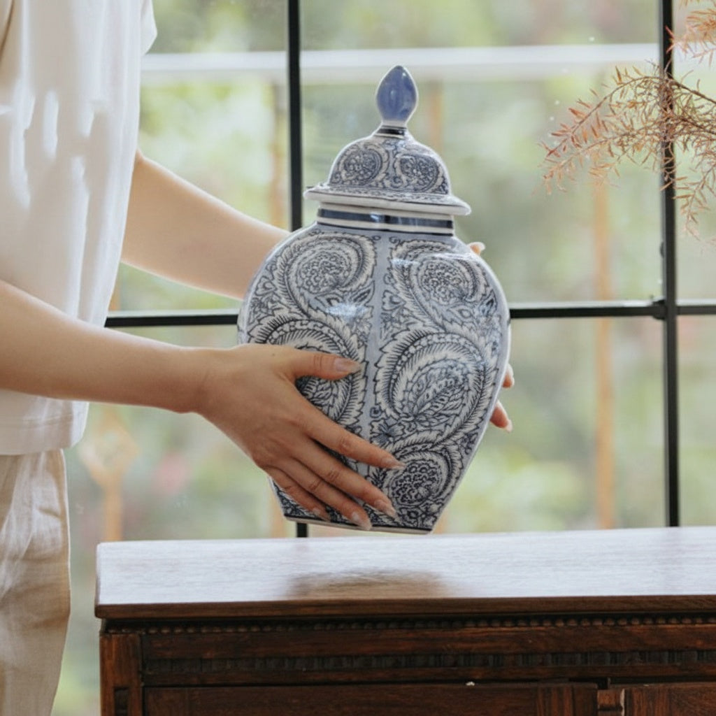 Hands holding blue and white porcelain ginger jar near window