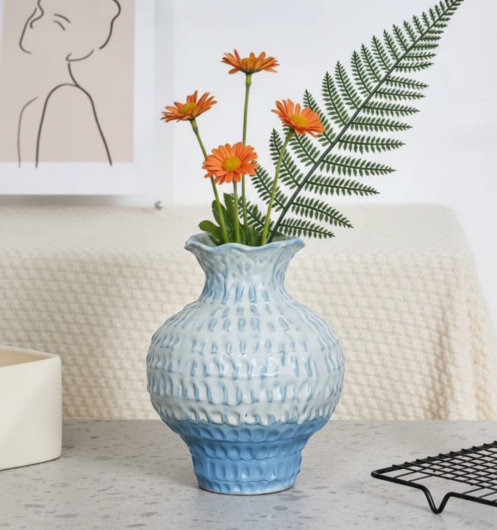 Textured blue ceramic vase holding orange flowers against white background