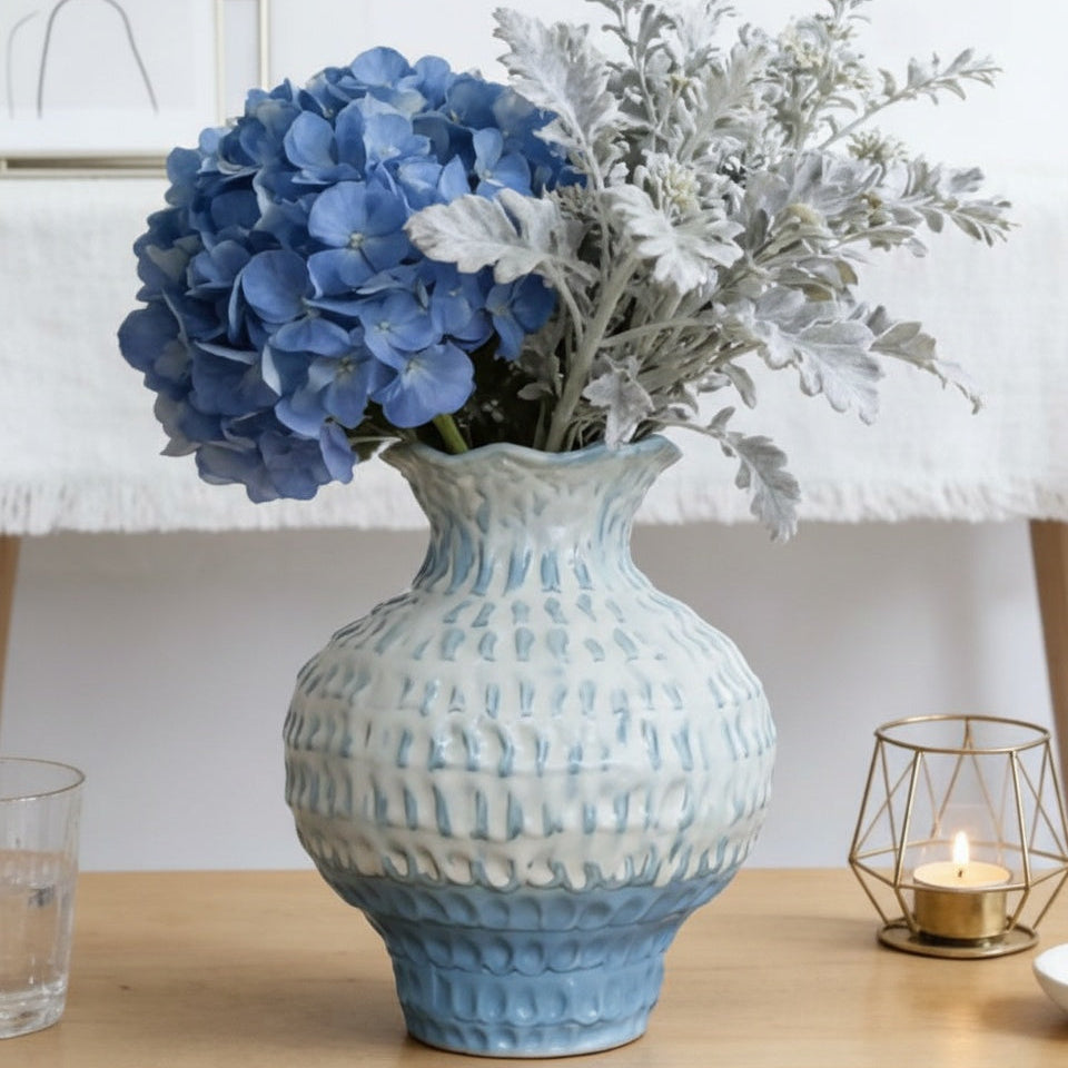 Glazed ceramic vase with blue hydrangeas on wooden surface