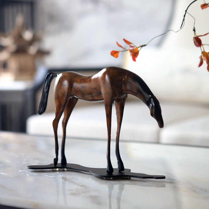 Side view of bronze stylized grazing horse sculpture on marble table