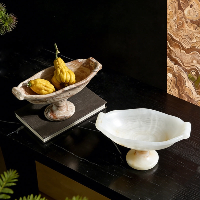 Beige cave stone pedestal bowl with fruit on dark table