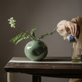 Celadon Ceramic Spherical Vase displaying delicate flowers on a table