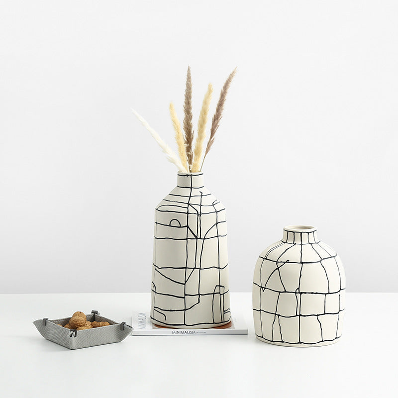 Two ceramic vases with black abstract grid lines on a white table