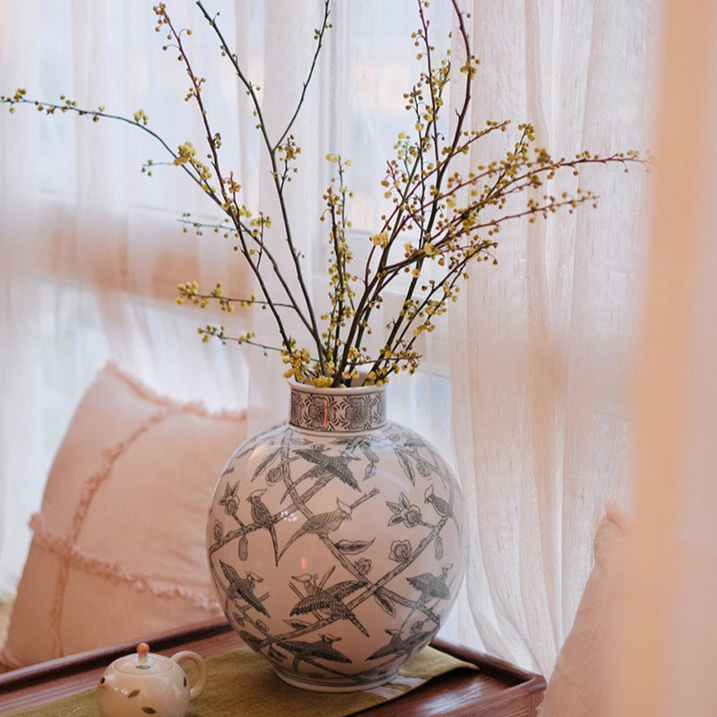Ceramic globular vase on window sill with branches