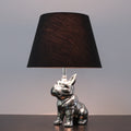 Front view of silver ceramic French bulldog table lamp with black shade lit