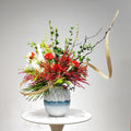 Studio front view of sculptural red floral arrangement in blue and white vase