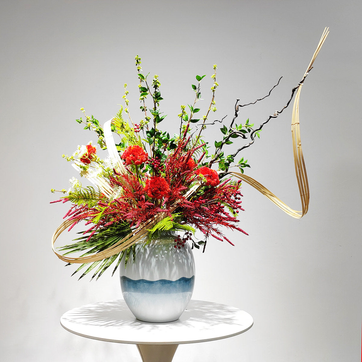 Studio front view of sculptural red floral arrangement in blue and white vase